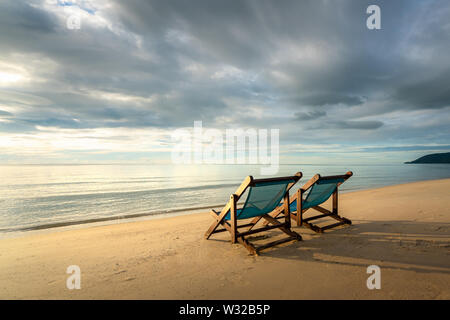 Due sedie a sdraio sulla spiaggia al tramonto con un mare tropicale sfondo. Viaggi e vacanze in estate al mare. Foto Stock