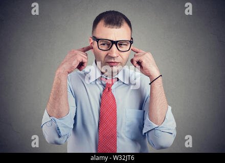 Infastiditi man looking grumpy tamponamento con le dita le orecchie disposta ad ascoltare chiunque. Foto Stock