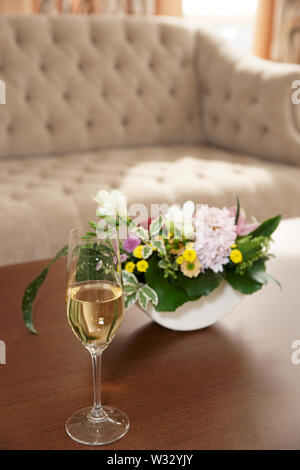 Bouquet e bicchiere di champagne sul tavolo nella lobby dell'hotel Foto Stock