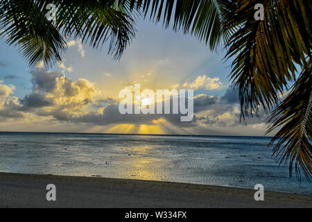 Vista atmosferica di un tramonto e obliqui raggi di sole sulla spiaggia, Aitutaki, Isole Cook, Polinesia Foto Stock