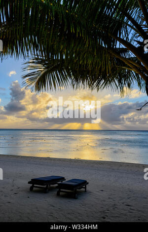 Vista verticale di un suggestivo tramonto e obliqui raggi di sole sulla spiaggia, Aitutaki, Isole Cook, Polinesia Foto Stock