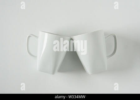 2 monocromatici bianchi tazze da caffè su sfondo bianco tintinnanti nel tifo con vuoto camera vuoto lo spazio per testo, copia o copia di spazio. Moderno vista superiore co Foto Stock