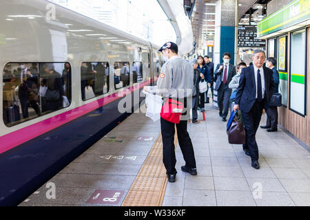 Tokyo, Giappone - Aprile 4, 2019: conduttore giapponese sulla piattaforma della stazione JR di Shinjuku stazione ferroviaria con treno superveloce shinkansen con la gente di affari businessma Foto Stock