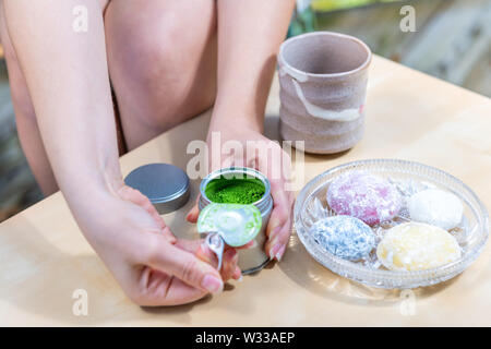 Verde matcha e mochi torte di riso giapponese dessert colorate wagashi con la donna ragazza apertura a mano Polvere di tè canister sul tavolo Foto Stock