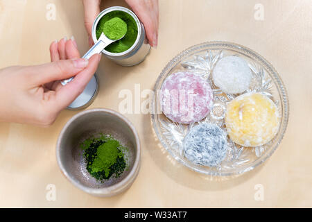 Verde matcha e mochi torta di riso dolce giapponese con la donna ragazza mano preparando il tè in polvere misurino su tavola Foto Stock