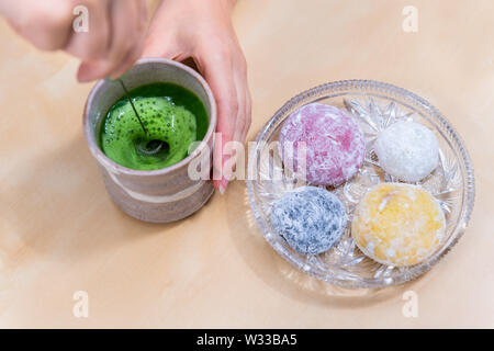 Donna agitazione Verde matcha tè con frother da mochi torta di riso giapponese wagashi dessert sul tavolo di legno Foto Stock