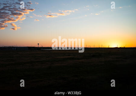 Snyder, Stati Uniti d'America vista della turbina eolica farm e linee di alimentazione in Texas campagna città industriale e un orizzonte con colorate di rosso tramonto Foto Stock