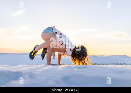 Donna esercizio facendo esercizio di corvo in equilibrio su mani nelle sabbie bianche dune monumento nazionale nel Nuovo Messico la vista del tramonto Foto Stock