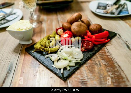 Antipasti antipasto ciliegio dolce mini peperoni ripieni di formaggio a pasta morbida feta e cipolle sulla piastra di ardesia. Foto Stock