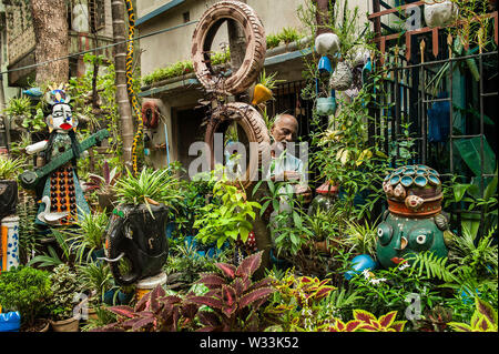 Kolkata. 12 Luglio, 2019. Giardiniere Partha Sarathi Ganguly, 65, si prende cura del suo giardino su strada in Kolkata, India su luglio, 11, 2019. Per annegamento e giardino decorazione ha riutilizzato scartato in plastica bottiglie di acqua, le bottiglie di vetro, contenitori di plastica, pneumatici, tubi di ciclo, filo elettrico e altre cose. Il giardino assorbe anche rifiuti umidi come compost come parte della gestione dei rifiuti. Credito: Xinhua /Tumpa Mondal/Alamy Live News Foto Stock