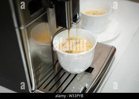 Caffè machinne versa del caffè in tazza bianca. Foto Stock