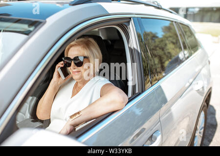 Bella senior business Donna che parla con il telefono mentre si guida un auto moderna. Concetto di persone attive durante l'età del pensionamento Foto Stock