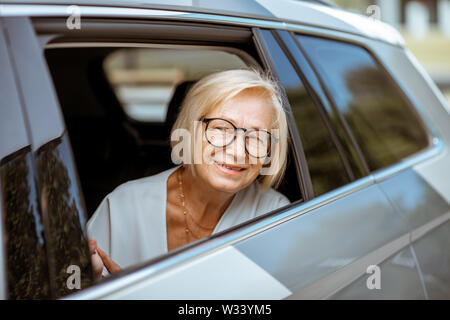 Ritratto di un felice senior business donna guardando fuori dalla finestra auto, viaggiare sul sedile posteriore di un taxi Foto Stock