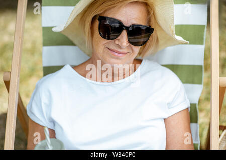 Ritratto di una bella donna senior sdraiato sul lettino, rilassante nel parco. Concetto di riposo e di vita spensierata sul pensionamento Foto Stock