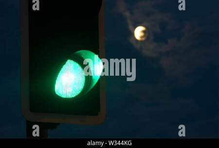 Un semaforo verde con una luna piena in background Foto Stock