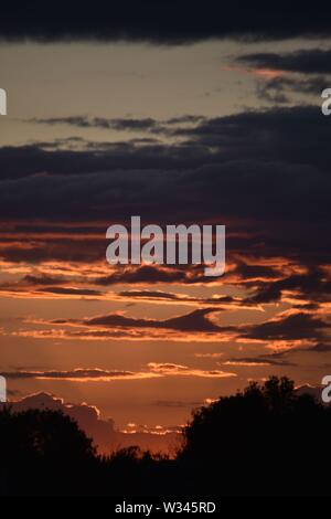 Tramonto sul flat suffolk campi con alcuni alberi in lontananza, viola scuro nuvole e un bello e caldo bagliore arancione nel cielo. Foto Stock