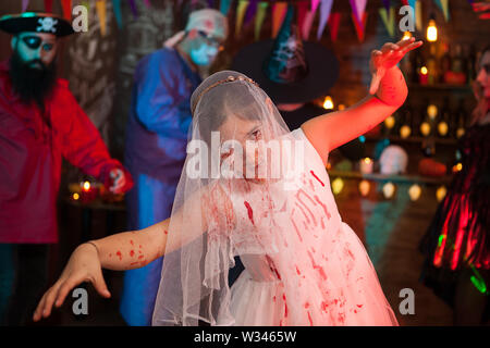 Scary bambina ad una festa di Halloween si veste come una sposa in abito di diserbo. Scary pirate in background. Foto Stock