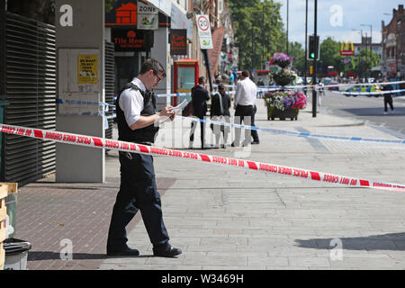 Un funzionario di polizia sulla scena di un accoltellato a Barking Road, Newham, a est di Londra. Forze di polizia sono chiamati a circa 0740 venerdì mattina per segnalazioni di un accoltellato e un uomo, credeva di essere nel suo 20s, è stato preso in un est di Londra in ospedale per il trattamento. Foto Stock