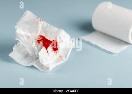 Una foto di usato sanguinosa carta igienica e una carta igienica rotolo sul fondo azzurro Foto Stock