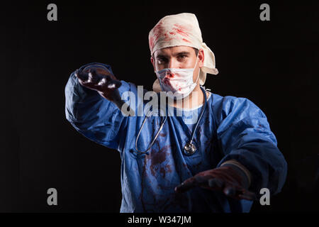 Ritratto giovane crazy medico vestiti di raggiungere con le sue mani su sfondo nero per halloween carnevale. Frustrati medico con sinistri l Foto Stock