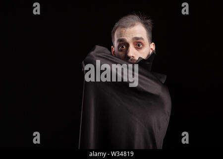 L uomo vestito in costume di Dracula per halloween nascondendo dietro il suo capo. Uomo malvagio in costume di Dracula. Spooky vampiro. Foto Stock