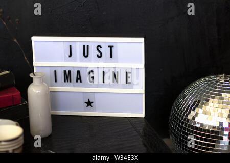 A led a luce casella con tipista font solo immaginare che sorge su di una tavola di cuoio accanto a un vaso di fiori e libri. Le sfocature Foto Stock