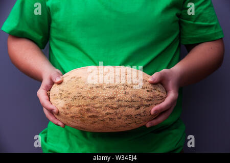 Il giovane uomo è in possesso di un grande ovale arancione melone maturo. Utili prodotti agricoli. Il raccolto dal campo Foto Stock