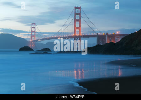 Vista panoramica classica del famoso Golden Gate Bridge visto da Scenic Baker Beach in bella luce dorata sera su un tramonto con cielo blu e nuvola Foto Stock