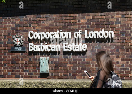 La Corporation of London Barbican Station Wagon signage su un edificio nel complesso con una donna il passaggio pedonale da Foto Stock