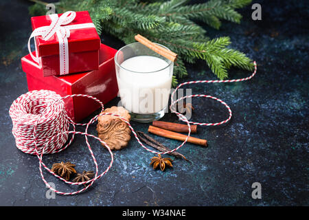 Deliziosi piatti fatti in casa natale gingerbread cookie con un bicchiere di latte, spezie, cannella e anice stelle, metall taglierine e dono su sfondo scuro. Foto Stock