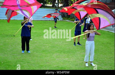 Giovani studenti in pratica la filatura di bandiera al di fuori sul prato all'università di Chulalongkorn nella zona centrale di Bangkok, Thailandia, Asia Foto Stock