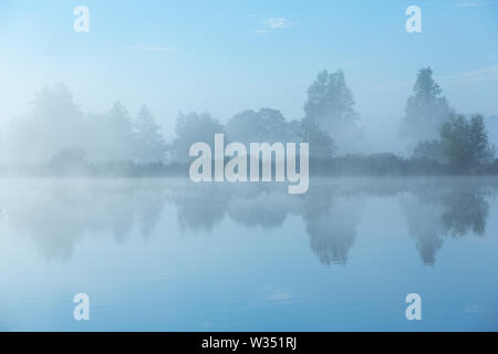 Una calma e tranquilla mattina presso il fiume con la nebbia in autunno e una bella riflessione in acqua - Drentse Aa, Drenthe, Paesi Bassi Foto Stock