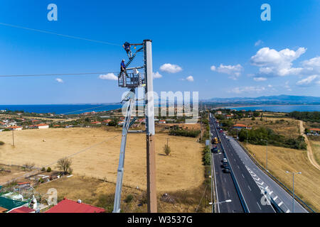 Calcidica, Grecia - Luglio 12, 2019: elettricisti sono arrampicata su poli elettrici da installare e riparare le linee di potenza dopo la violenta tempesta che ha colpito il t Foto Stock