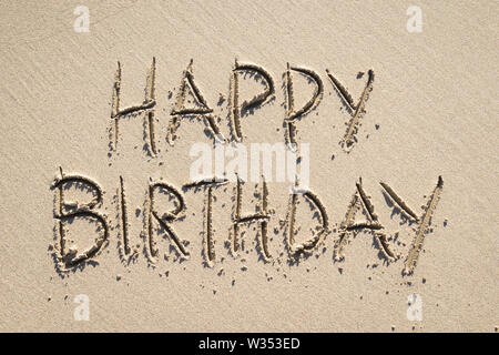 Buon compleanno messaggio scritto a mano in caratteri maiuscoli nella spiaggia di Liscia sabbia sotto la luce diretta del sole Foto Stock