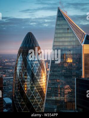 I raggi dorati di sunrise di colpire il lato del cetriolino e edifici di bisturi nella città di Londra Foto Stock