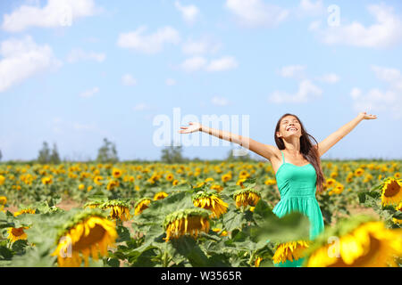 Felice estate spensierata ragazza nel campo di semi di girasole in primavera. Allegro e multirazziale caucasico asiatica giovane donna gioiosa, sorridente con le braccia sollevate verso l'alto. Foto Stock