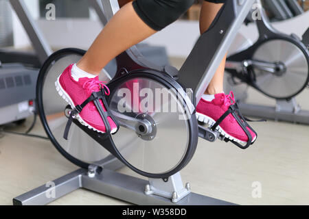 Cyclette con ruote di filatura. Donna escissione bike nel centro fitness. closeup di pedali. Professional centro fitness attrezzatura. Foto Stock