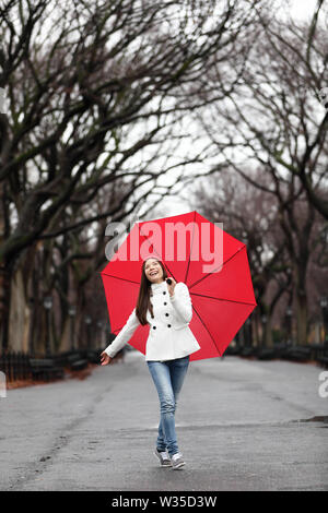 Donna con ombrello in caduta di pioggia o d'inverno. Sorridenti ragazza camminare allegro con ombrello rosso a Central Park, Manhattan, New York City, Stati Uniti d'America. Foto Stock