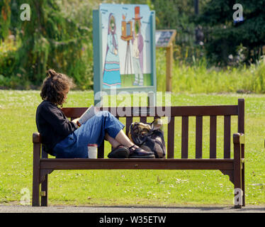 Glasgow, Scotland, Regno Unito 12 luglio, 2019. Regno Unito Meteo Sunny ha visto il ritorno di estate con bella ragazza su banco del libro di lettura di fronte snapshot Photo Booth per la botanica nella sistemazione di west end della città con i suoi giardini botanici e ben tenuto parco preferito per i turisti. Credito: Gerard Ferry/ Alamy Live News Foto Stock