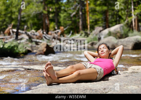 Escursionismo donna sola rilassante dormendo dal fiume creek in natura. Stanco escursionista in appoggio sdraiato all'aperto prendendo una pausa da escursione. Giovane donna asiatica nella foresta nel parco nazionale di Yosemite in California, Stati Uniti d'America. Foto Stock