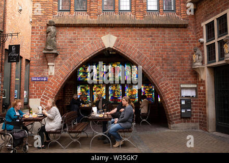 Le finestre di vetro macchiate e tavoli esterni con persone bere e mangiare presso il Bar Freytag su Böttcherstrasse nella zona centrale di Bremen, Germania. Foto Stock