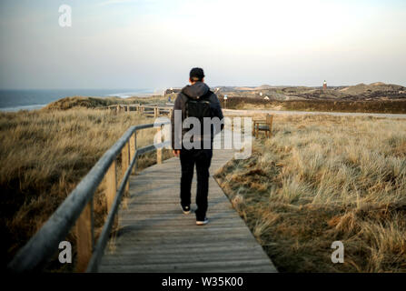 Sylt, Germania. 18 Febbraio, 2019. Un giovane uomo cammina su una passerella in legno attraverso le dune sull isola di Sylt. Sylt è la più grande del nord Isola Frisone in Germania. Credito: Britta Pedersen/dpa-Zentralbild/ZB/dpa/Alamy Live News Foto Stock