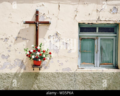 Una vecchia casa diroccata parete con esfoliate di color crema in gesso, a destra di una finestra con verde chiuso persiane di legno. Sul lato sinistro accanto al Foto Stock