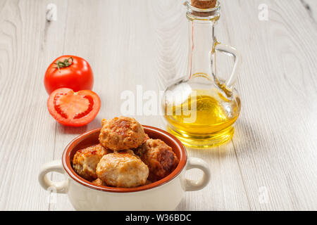 Fritte costolette di carne in ceramica Soup Bowl, pomodori rossi e bottiglia di vetro con olio di semi di girasole su grigio di tavole di legno. Foto Stock