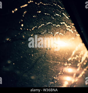 Bellissimo sfondo con caduta di pioggia sulla finestra, semaforo con close up shoot del vetro per auto a notte rendere bokeh in ciano e giallo Foto Stock