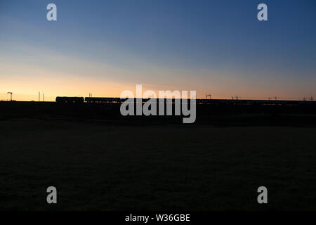 GB classe di merci su rotaie 92 locomotiva elettrica passando Greenholme, Cumbria, stagliano con il sorgere del sole con la pianura Serco Caledonian Sleeper Foto Stock