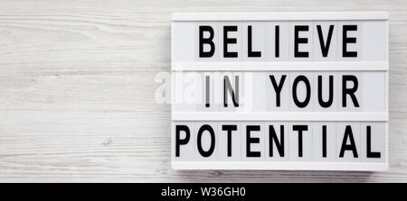 "Credo in il vostro potenziale di parole su un lightbox su un bianco superficie in legno, vista dall'alto. Spazio per il testo. Foto Stock