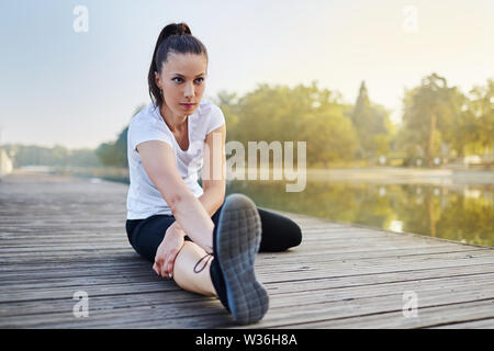 Ritratto di giovane donna stretching vicino al lago prima di fare jogging al mattino Foto Stock