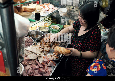 Donna vietnamita vendere il pane del Vietnam sul carrello di notte street food, alimentari farcite con carne di maiale, bologna, decapare, un famoso e popolare che cibo a buon mercato Foto Stock