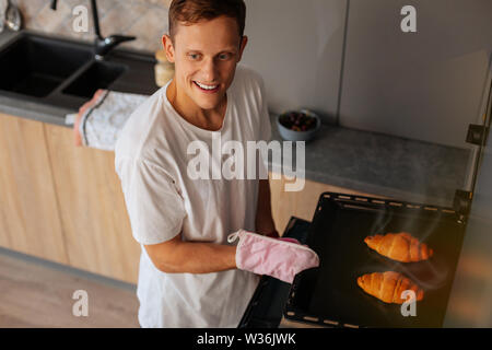 Il marito amorevole per la cottura tenendo il vassoio con croissant Foto Stock